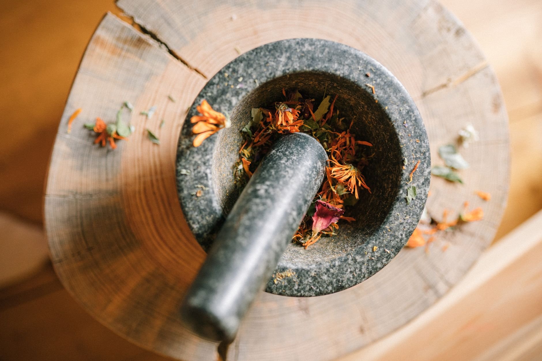 Close-up of a granite mortar and pestle grinding dried flowers on a wooden surface.