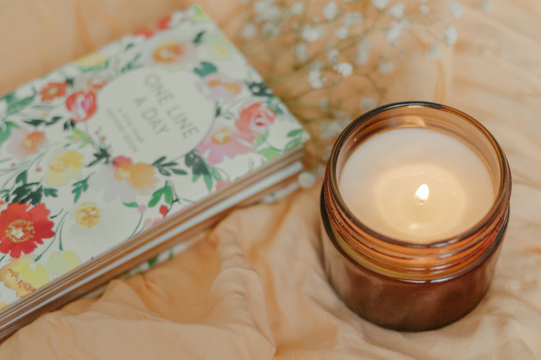 Floral journal and warm candle on soft fabric, creating a cozy atmosphere.
