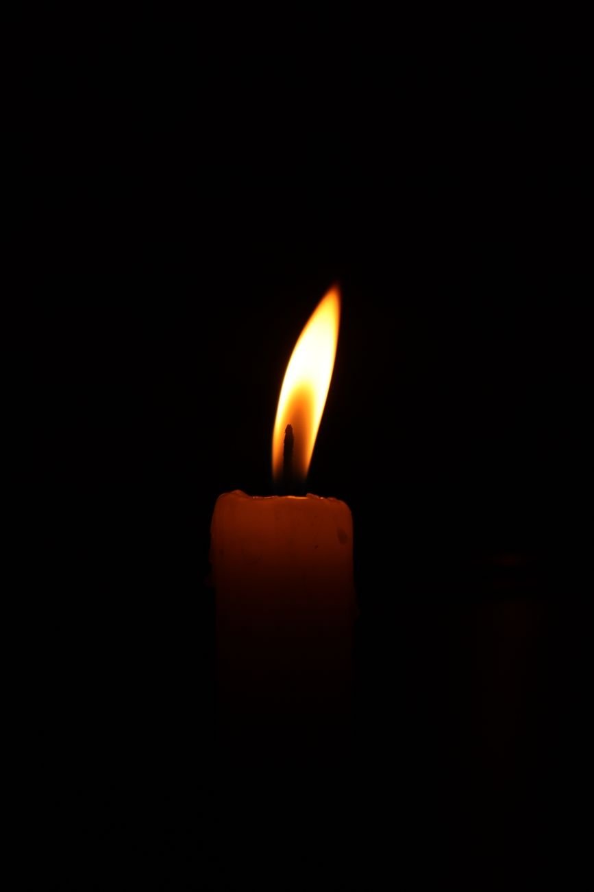 Close-up of a lit candle casting warm light in darkness, creating a serene atmosphere.